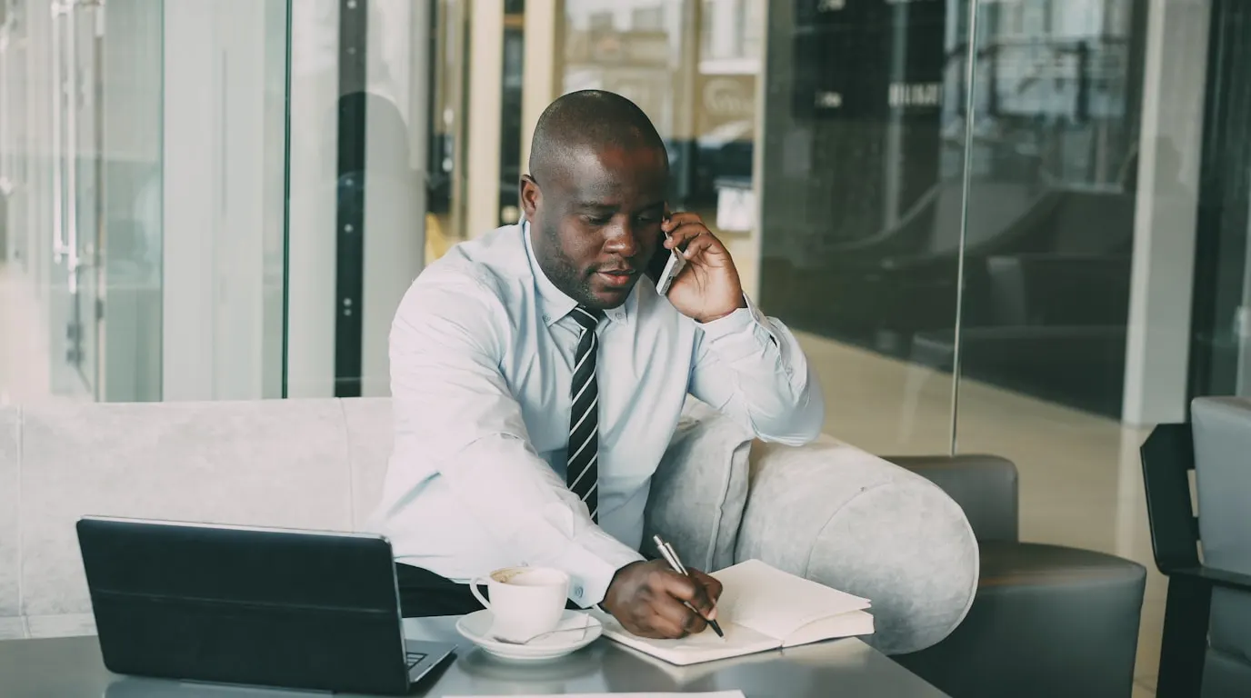 A business owner on a phone call taking notes in a notebook, testing how an AI receptionist handles a real conversation