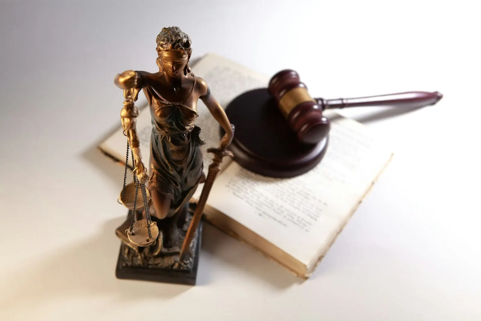 A small statue of Lady Justice holding scales beside a wooden gavel resting on an open book
