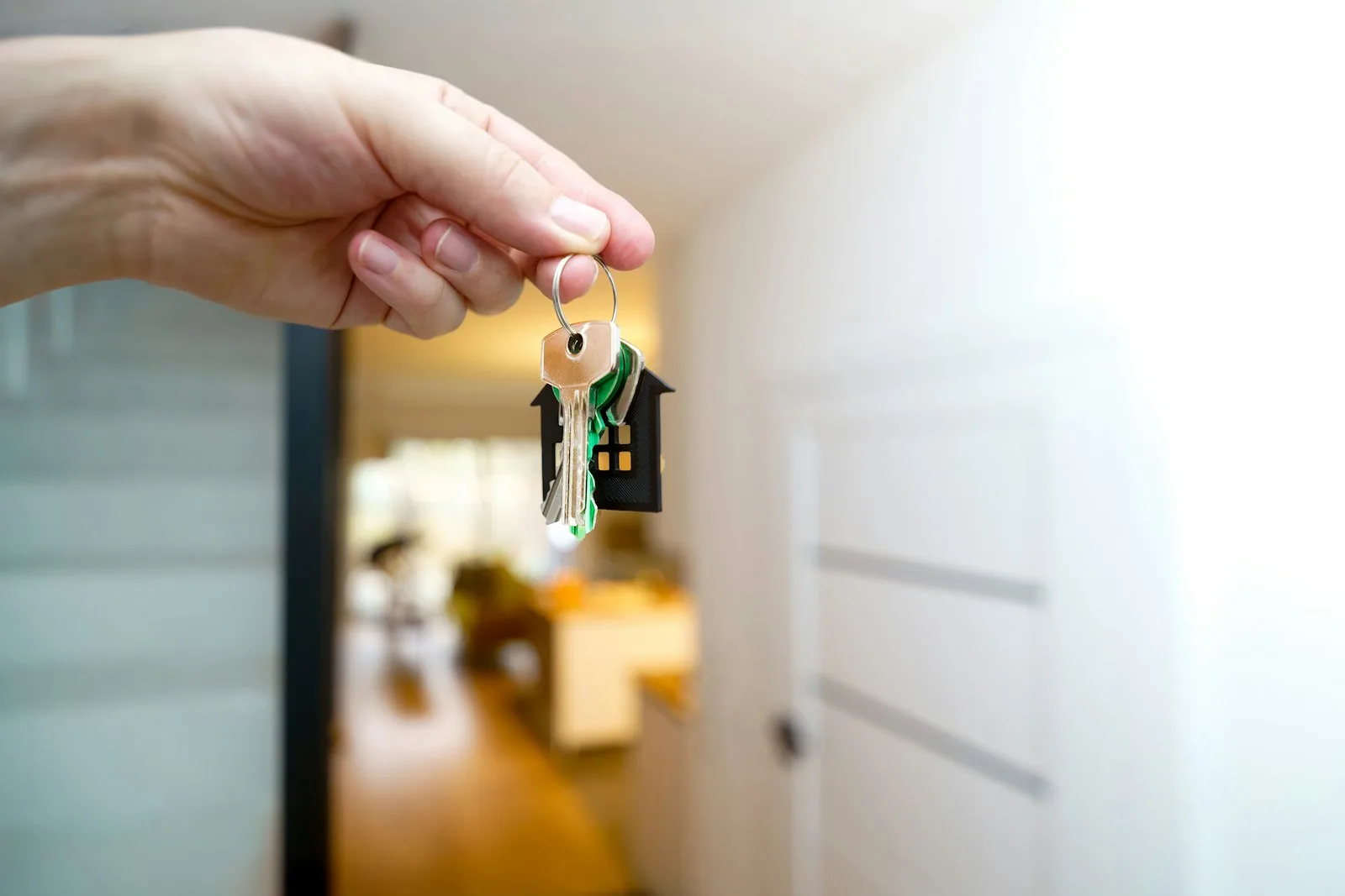 A hand holding a set of house keys with a small house-shaped keyring in the doorway of a new home, representing a closed real estate deal